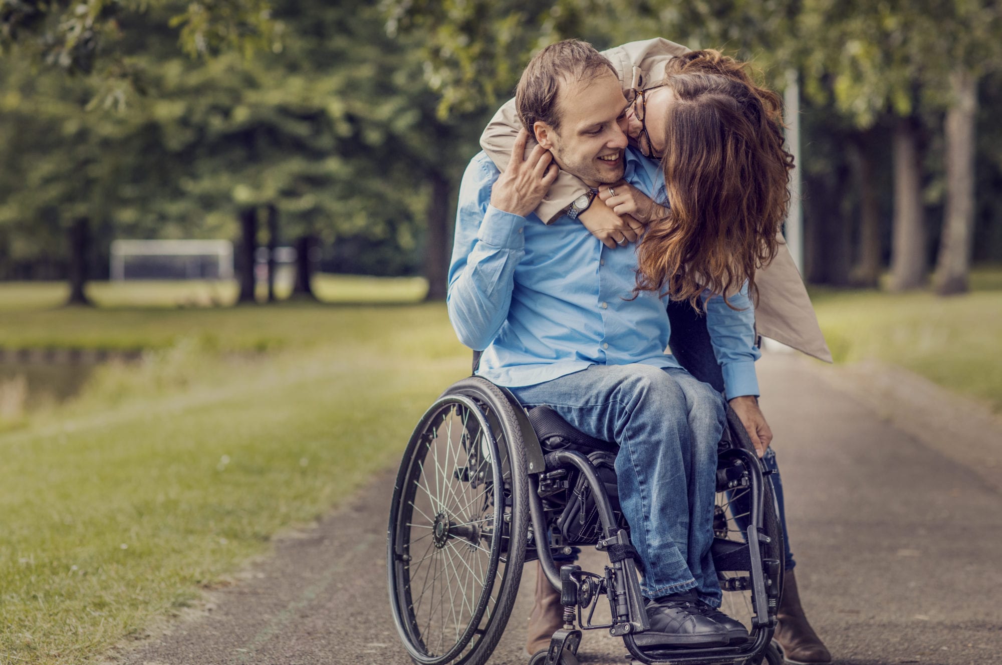 Wheelchair using young man and his girlfriend walking together through a city park